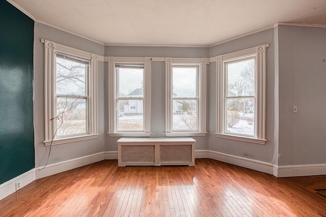 spare room with baseboards, ornamental molding, radiator heating unit, and light wood-style floors