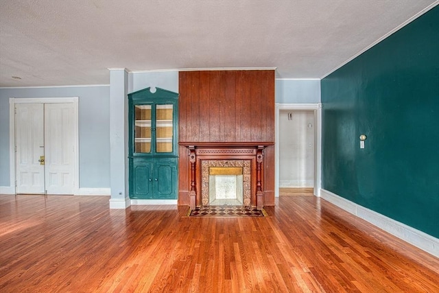 unfurnished living room with crown molding, a fireplace, baseboards, and wood finished floors