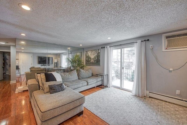 living room featuring baseboard heating, wood-type flooring, a wall unit AC, and a textured ceiling