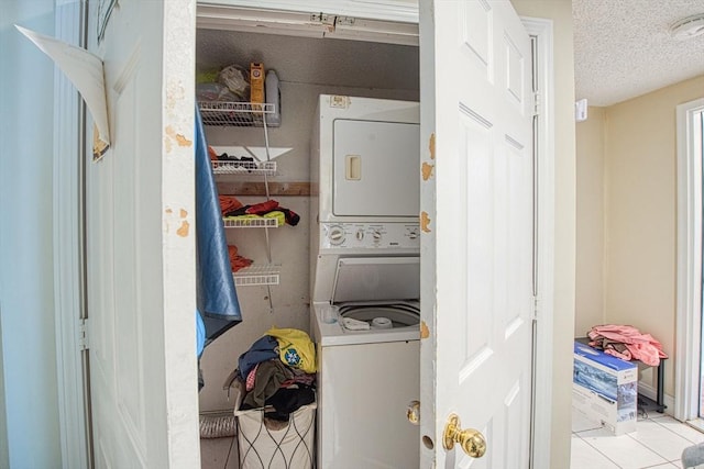 laundry area featuring stacked washer / drying machine, light tile patterned floors, and a textured ceiling