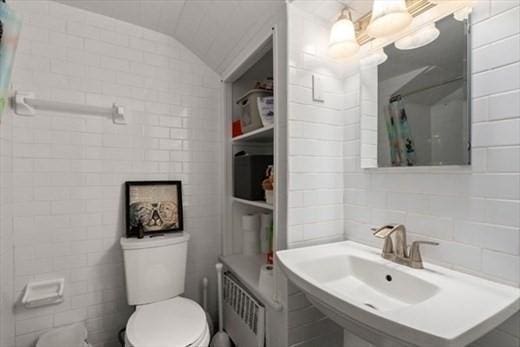 bathroom featuring lofted ceiling, toilet, sink, tile walls, and curtained shower