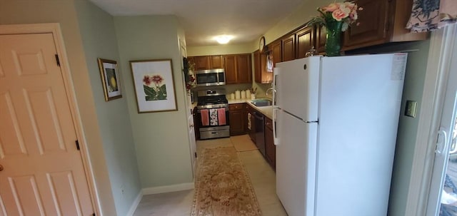 kitchen featuring stainless steel appliances, a sink, light countertops, and baseboards