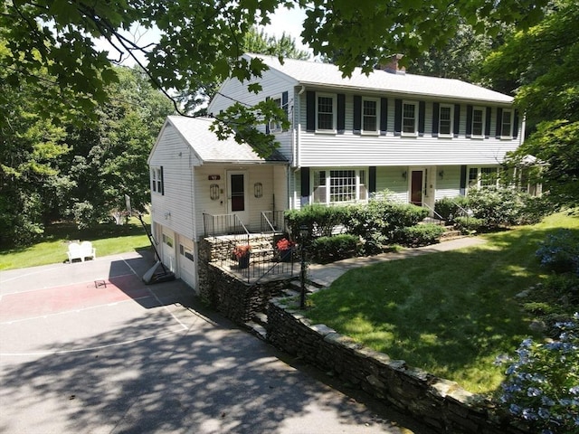 colonial inspired home featuring a garage, a chimney, driveway, and a front lawn
