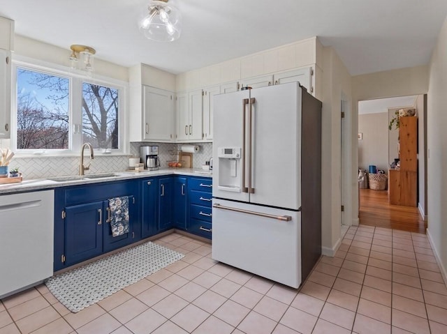 kitchen featuring blue cabinetry, tasteful backsplash, a sink, light countertops, and white appliances