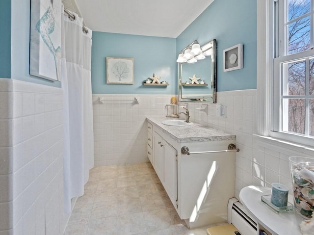 full bath with a wainscoted wall, plenty of natural light, a baseboard heating unit, and tile walls