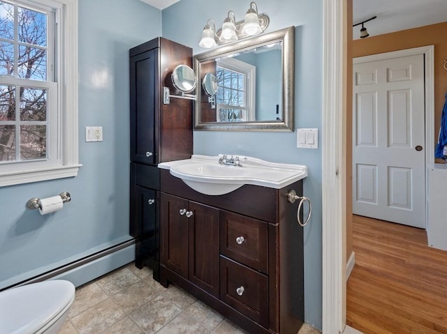 bathroom with toilet, a wealth of natural light, baseboard heating, and vanity