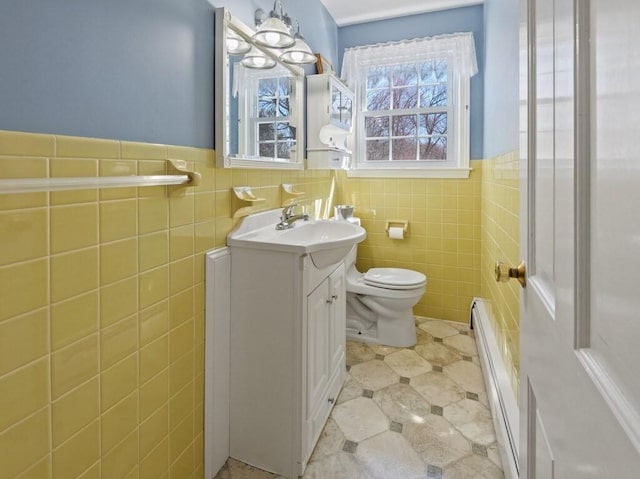 bathroom featuring tile walls, wainscoting, vanity, a baseboard radiator, and toilet