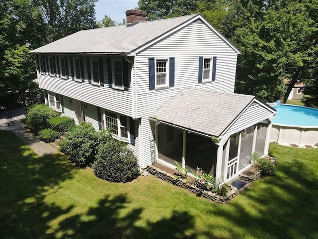 rear view of house featuring a sunroom, roof with shingles, an outdoor pool, and a chimney