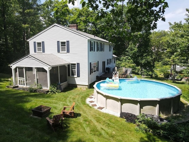 rear view of property featuring an outdoor pool, a chimney, a sunroom, an outdoor fire pit, and a yard