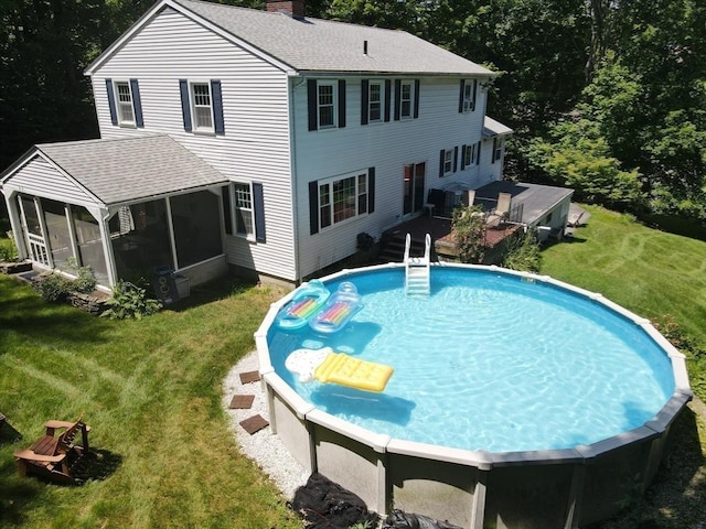 rear view of house with a sunroom, a shingled roof, a lawn, and a chimney