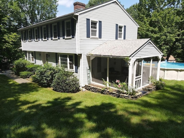 rear view of house with an outdoor pool, roof with shingles, a chimney, a sunroom, and a yard
