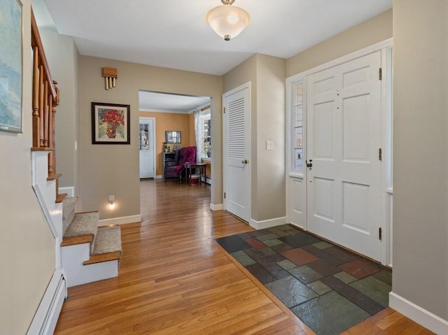 foyer entrance with stairway, baseboards, a baseboard radiator, and wood finished floors