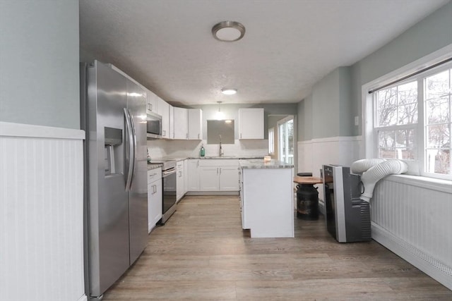 kitchen with stainless steel appliances, sink, white cabinets, a center island, and light hardwood / wood-style floors