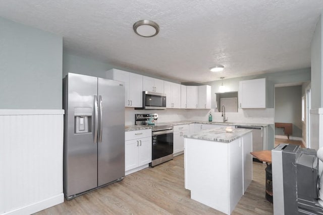 kitchen with a textured ceiling, stainless steel appliances, white cabinets, light hardwood / wood-style floors, and a kitchen island