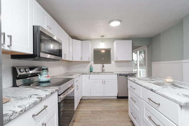 kitchen with white cabinets, hanging light fixtures, sink, appliances with stainless steel finishes, and light hardwood / wood-style floors