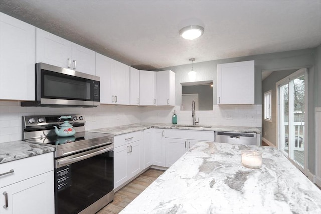 kitchen featuring pendant lighting, white cabinets, sink, light stone countertops, and stainless steel appliances