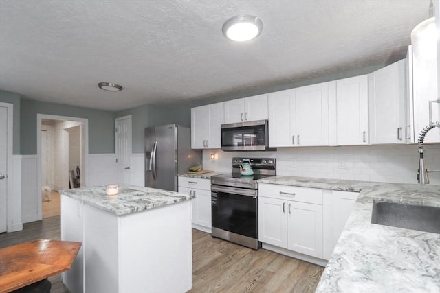 kitchen with white cabinets, sink, light stone countertops, appliances with stainless steel finishes, and a kitchen island