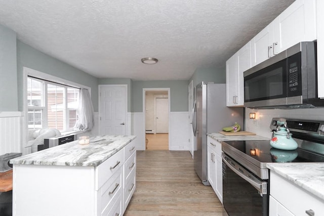 kitchen with a textured ceiling, appliances with stainless steel finishes, a kitchen island, light stone counters, and white cabinetry