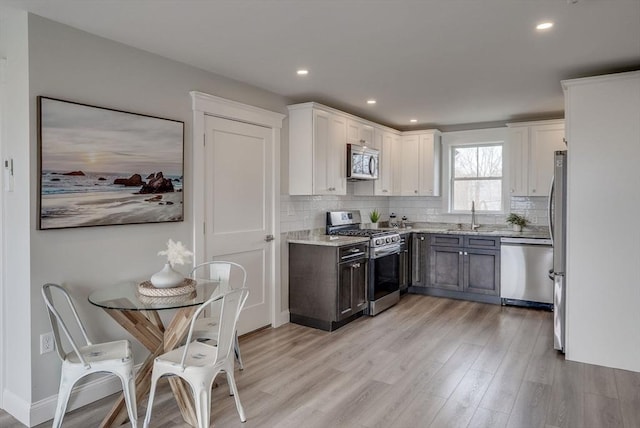 138 Flash Rd Unit 1, Nahant, MA 01908 - kitchen with stainless steel appliances, light wood-style floors, tasteful backsplash, white cabinets, and light stone countertops