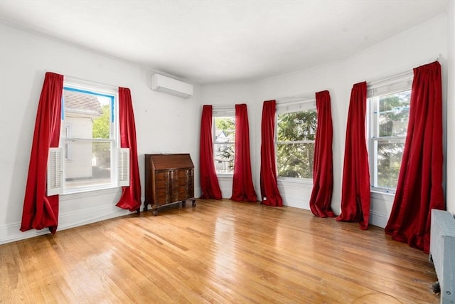 spare room with a wall mounted air conditioner, light wood finished floors, radiator heating unit, and plenty of natural light