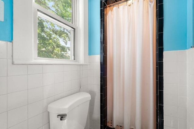 bathroom with tile walls, curtained shower, toilet, and wainscoting