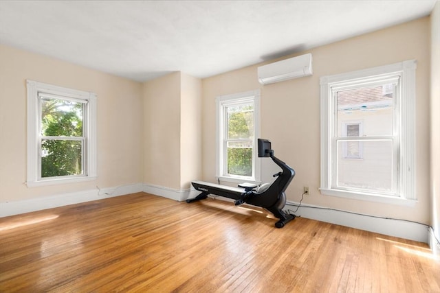 exercise room featuring a wall mounted air conditioner, hardwood / wood-style flooring, and baseboards