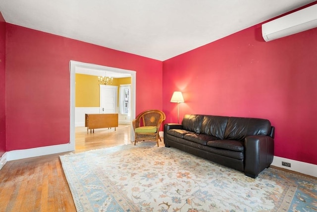 living room with a wall mounted AC, a chandelier, baseboards, and wood finished floors