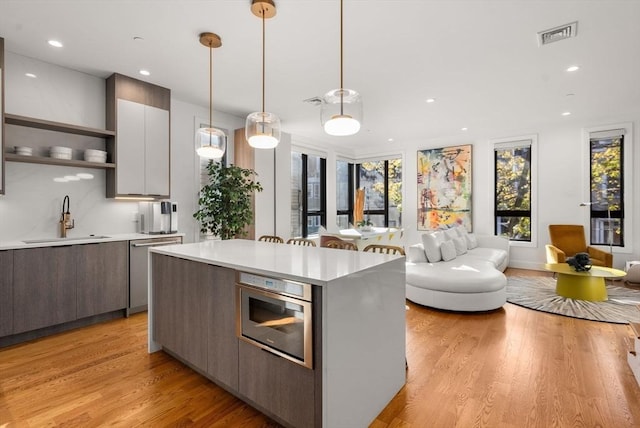 kitchen with pendant lighting, white cabinets, sink, light hardwood / wood-style flooring, and a kitchen island