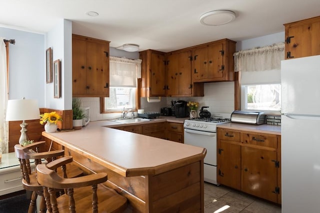 kitchen with light countertops, white appliances, a peninsula, and a sink