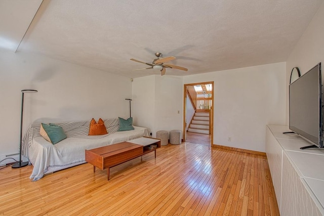 living room featuring baseboards, ceiling fan, light wood-style flooring, and stairway