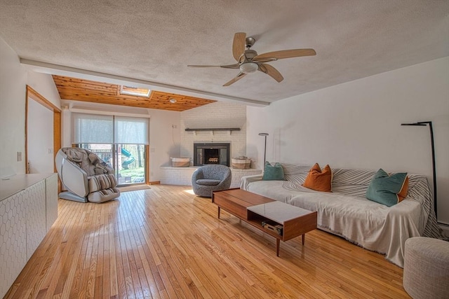living room featuring a textured ceiling, light wood-style flooring, ceiling fan, and a fireplace