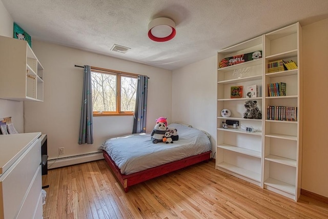 bedroom featuring visible vents, a textured ceiling, light wood-style flooring, and a baseboard heating unit