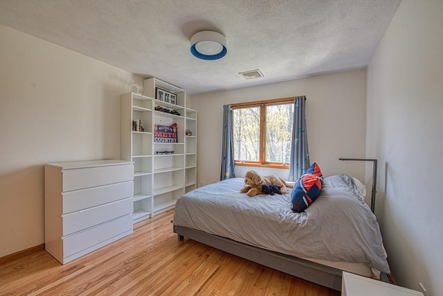 bedroom featuring visible vents, a textured ceiling, light wood-style flooring, and baseboards