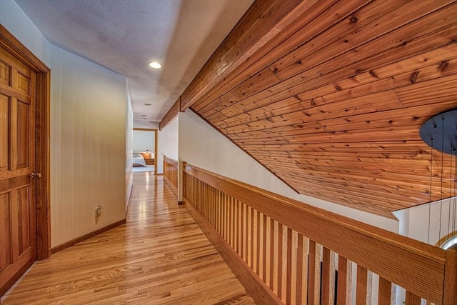 hall featuring light wood-type flooring, recessed lighting, baseboards, and an upstairs landing