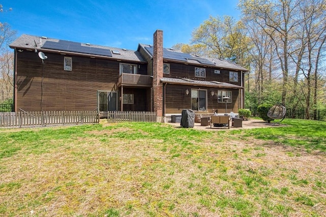 rear view of house featuring a chimney, a lawn, a patio area, a fenced backyard, and roof mounted solar panels