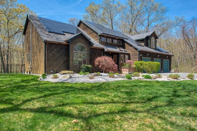 view of front of property with a garage, roof mounted solar panels, fence, and a front yard