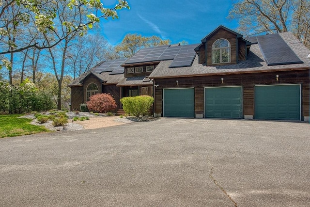 view of front of home with a garage, aphalt driveway, a shingled roof, and solar panels