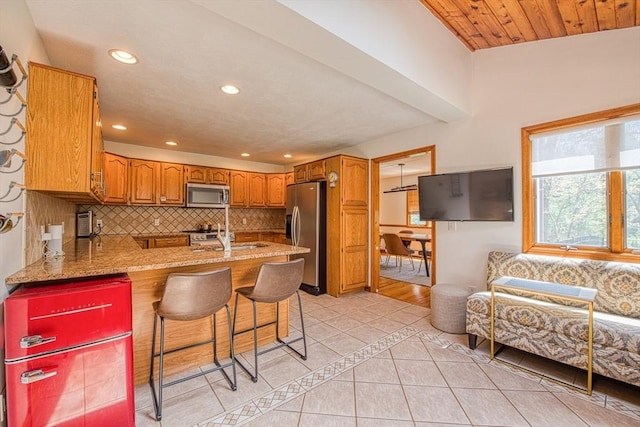 kitchen featuring appliances with stainless steel finishes, brown cabinetry, a peninsula, decorative backsplash, and light tile patterned floors