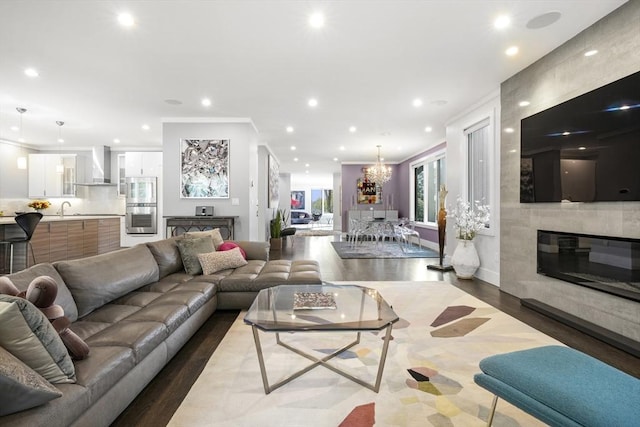 living area with a large fireplace, ornamental molding, wood finished floors, a notable chandelier, and recessed lighting