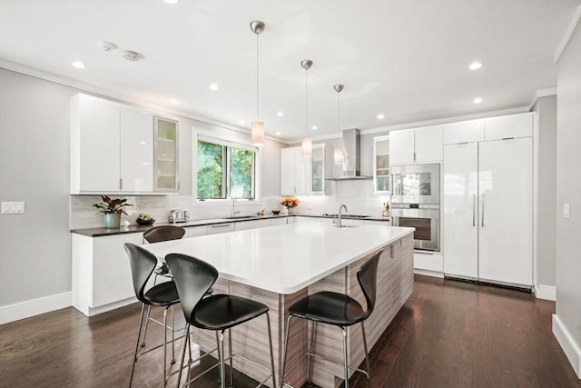 kitchen featuring dark countertops, hanging light fixtures, white cabinets, paneled built in refrigerator, and wall chimney exhaust hood