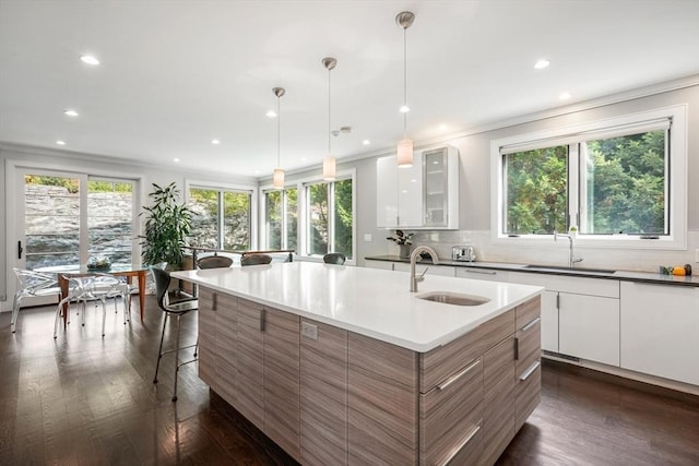 kitchen featuring a kitchen island with sink, glass insert cabinets, white cabinets, and a sink