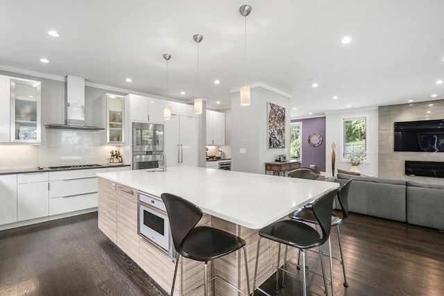 kitchen featuring light countertops, glass insert cabinets, white cabinets, modern cabinets, and wall chimney exhaust hood