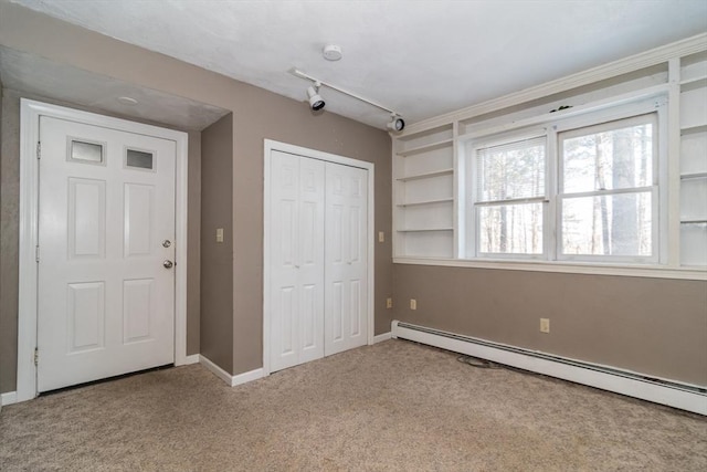 unfurnished bedroom with track lighting, carpet floors, a closet, and a baseboard heating unit