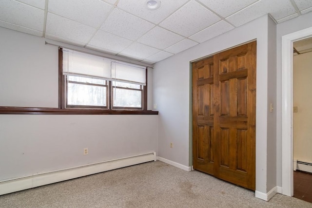 unfurnished bedroom with light carpet, a baseboard radiator, and a drop ceiling