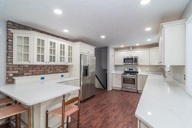 kitchen with sink, a breakfast bar area, white cabinetry, stainless steel appliances, and kitchen peninsula