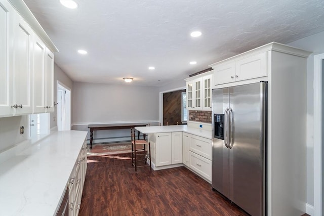 kitchen with dark wood-type flooring, a kitchen bar, light stone counters, stainless steel fridge, and white cabinets