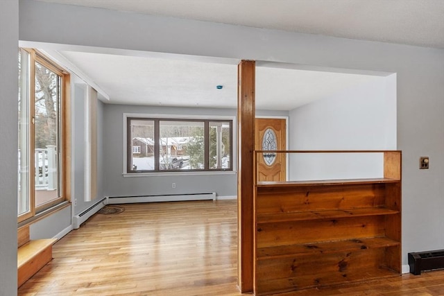 empty room featuring a baseboard heating unit, light wood-type flooring, and baseboards