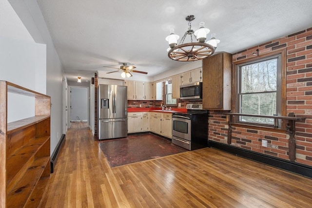 kitchen with wood finished floors, decorative light fixtures, cream cabinets, stainless steel appliances, and a sink