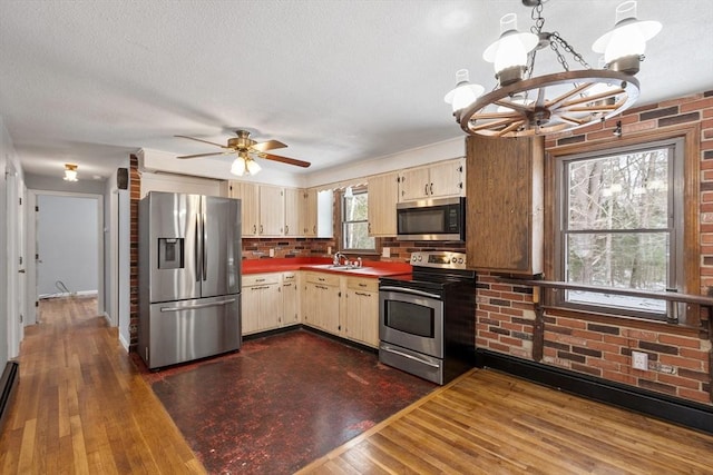 kitchen with dark wood finished floors, stainless steel appliances, decorative backsplash, cream cabinets, and a sink