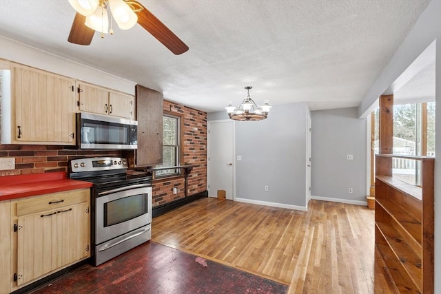 kitchen featuring dark countertops, light brown cabinetry, appliances with stainless steel finishes, a textured ceiling, and baseboards